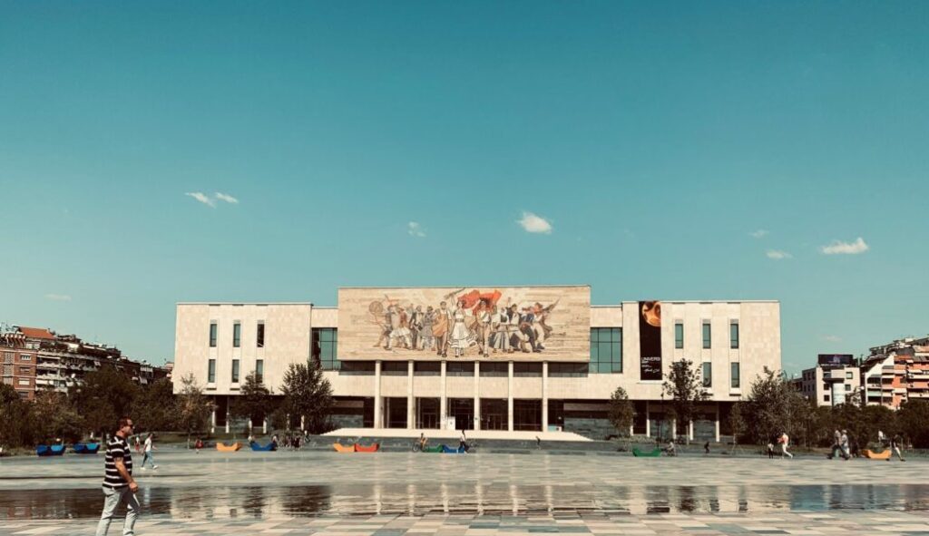 A large building with a mosaic mural depicting a crowd of people, located in Skanderbeg Square, Tirana, Albania.